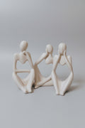 Three minimalist ceramic figurines of seated female figures in warm off-white, arranged side-by-side on a light surface.