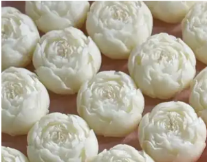 A close-up of multiple round, pale off-white flower-shaped confectionery items arranged closely together on a warm pinkish-brown surface.