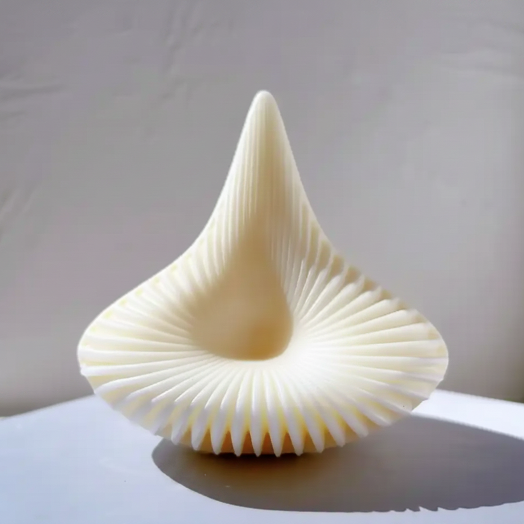 A sculptural, ribbed candle ivory tone, photographed on a white surface against a light neutral wall.