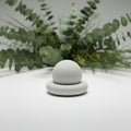 A minimalist white ceramic or stone decorative object with a rounded dome on a circular base.