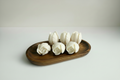 Six sculpted tulip shaped wax melts arranged on a dark wooden tray on a plain white background. 